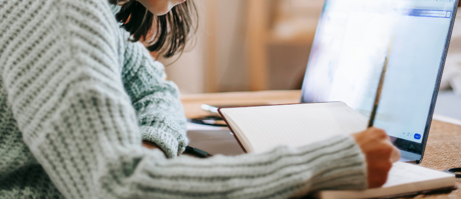 A girl doing some work with the computer and a book next to it